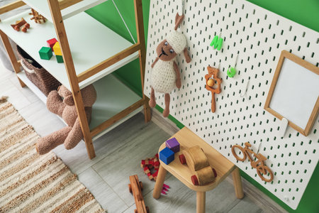 Shelving unit with toys and pegboard on stool near green wallの写真素材