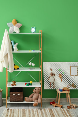 Shelving unit with toys and pegboard on stool near green wallの写真素材