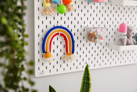 Pegboard with children's toys and bottles hanging on light wall in roomの写真素材