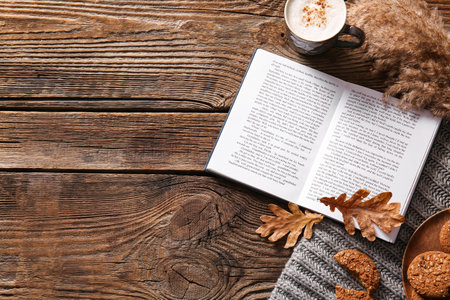 Book, cup of coffee, cookies and autumn decor on wooden background