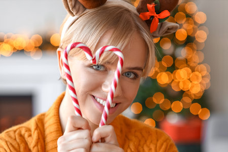 Beautiful young woman with candy canes at home on Christmas eveの写真素材