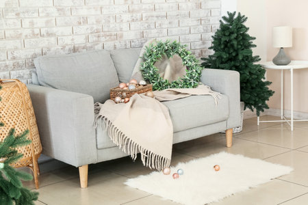 Sofa with Christmas balls and mistletoe wreath near brick wall