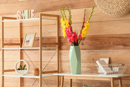 Vase with beautiful gladiolus flowers on table near wooden wallの写真素材