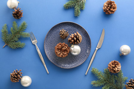 Beautiful table setting with Christmas balls, fir branches and cones on blue backgroundの写真素材