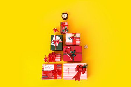 Christmas tree made of gift boxes and alarm clock on yellow backgroundの写真素材