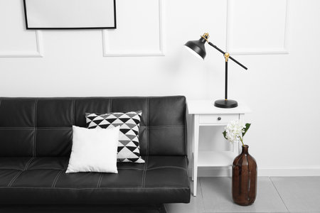 Glowing black lamp on table and sofa near light wallの写真素材