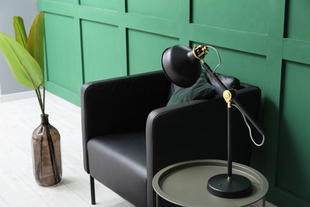 Black lamp on table and armchair near green wallの写真素材