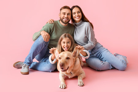 Happy parents with little daughter and Labrador dog on pink backgroundの写真素材