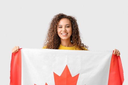 Beautiful young African-American woman with Canadian flag on light backgroundの写真素材