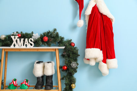 Decorated table with word XMAS and Santa Claus costume and boots on color backgroundの写真素材