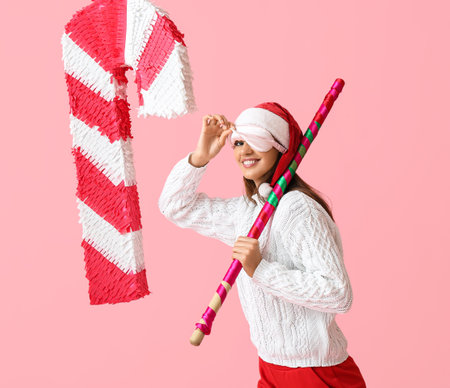 Beautiful woman in Santa hat and with candy cane pinata on color backgroundの写真素材