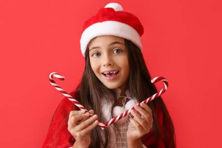 Cute little girl in Santa hat and with candy canes on color backgroundの写真素材