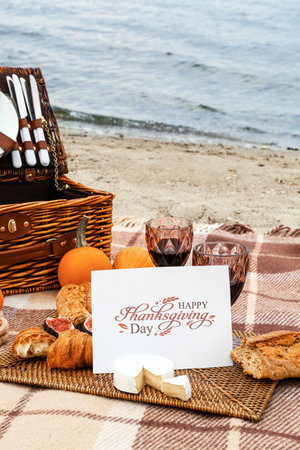 Glasses of wine, delicious food and card with text HAPPY THANKSGIVING DAY on beachの写真素材