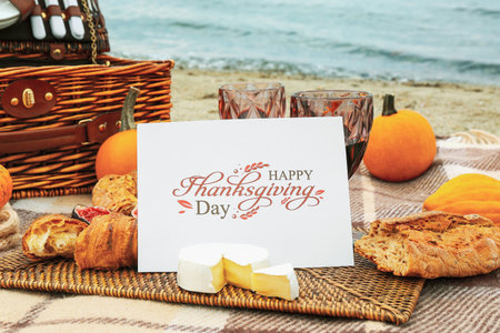 Glasses of wine, delicious food and card with text HAPPY THANKSGIVING DAY on beach, closeupの写真素材