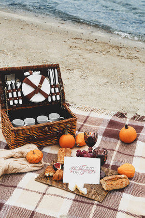 Basket with dishes, glasses of wine, delicious food and card with text HAPPY THANKSGIVING DAY on beachの写真素材