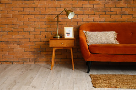 Table with golden lamp, picture and red sofa near brick wallの写真素材