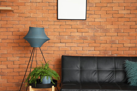 Table with houseplant, standing lamp and couch near brick wallの写真素材