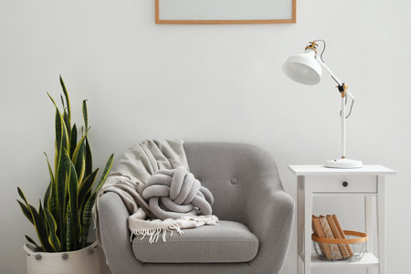 Stylish lamp on table, armchair and houseplant near light wallの写真素材