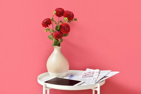 Vase with beautiful dahlias, tablet computer and newspapers on table near color wallの写真素材