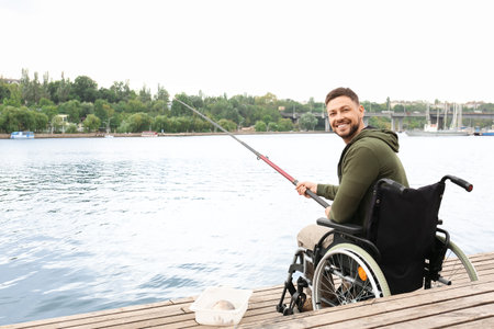 Man in wheelchair fishing on riverの写真素材