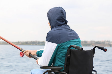 Man in wheelchair fishing on riverの写真素材