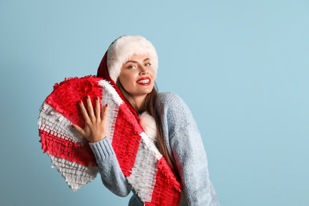 Pretty young woman in Santa hat with candy cane pinata on blue backgroundの写真素材