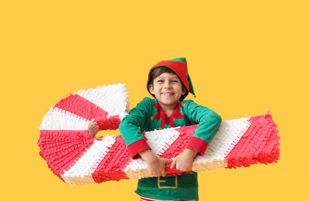 Cute little boy dressed as elf with candy cane pinata on color backgroundの写真素材