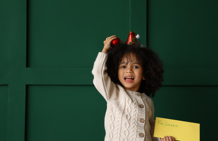 Cute African-American girl with letter to Santa on color backgroundの写真素材