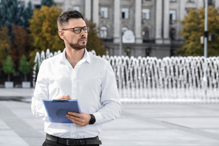 Stylish businessman writing in clipboard on city squareの写真素材