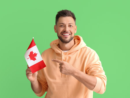 Happy young man pointing at flag of Canada on green backgroundの写真素材