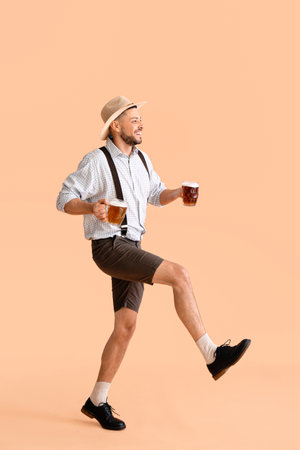 Young man in traditional German clothes with beer on beige backgroundの写真素材