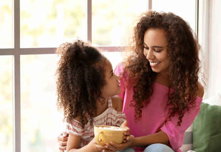 Little African-American girl and her mother with mug of hot cocoa at homeの写真素材