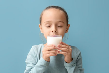 Cute girl drinking milk on blue backgroundの写真素材
