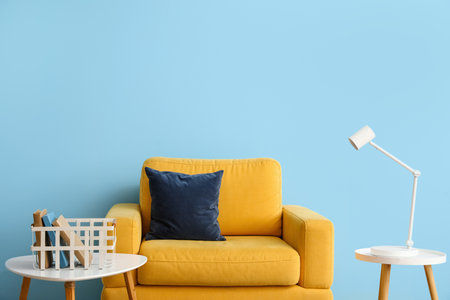 Yellow armchair, coffee tables with books and lamp near blue wallの写真素材