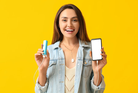 Young woman with phone and power bank on color backgroundの写真素材
