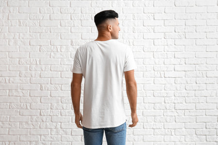 Handsome young man in stylish t-shirt on white brick background, back view