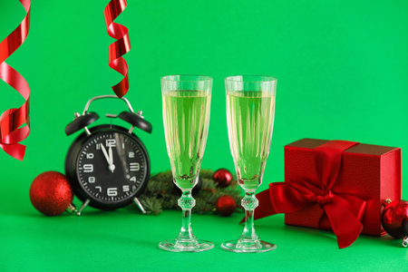 Glasses of champagne, Christmas gift, alarm clock and serpentine on green backgroundの写真素材