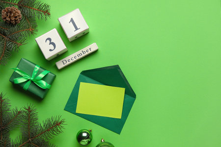 Cube calendar with date of DECEMBER 31, fir branches, gift box and blank card on green backgroundの写真素材