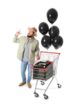 Handsome man with Black Friday shopping bags in carts and balloons on white backgroundの写真素材