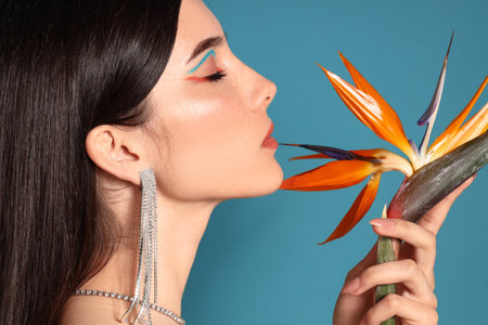 Beautiful young woman with strelitzia flower on color background