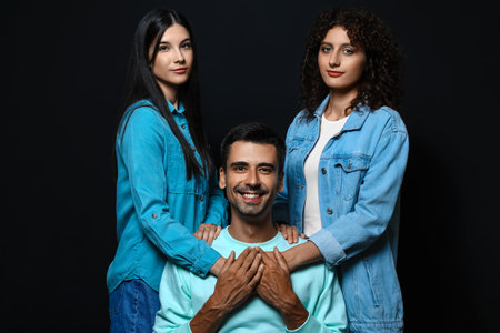 Man and two beautiful women on dark background. Polyamory conceptの写真素材