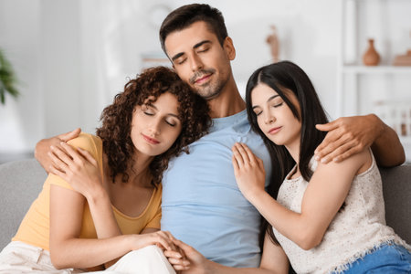 Man and two beautiful women sitting on sofa. Polyamory conceptの写真素材
