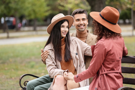 Man and two beautiful women sitting on bench in park. Polyamory conceptの写真素材