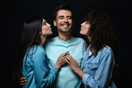 Man and two beautiful women on dark background. Polyamory conceptの写真素材