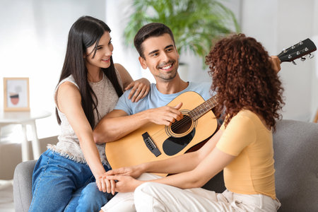 Man playing guitar for two beautiful women at home. Polyamory conceptの写真素材