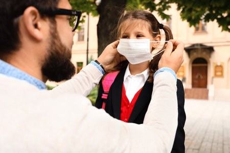 Man helping his little daughter to put on medical mask before schoolの写真素材