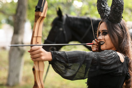 Beautiful woman dressed for Halloween with bow in the forestの写真素材
