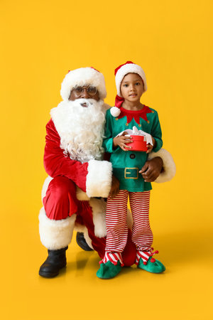 Cute little elf with gift and Santa Claus on yellow backgroundの写真素材