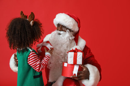 Cute little elf with Santa Claus and gifts on red backgroundの写真素材