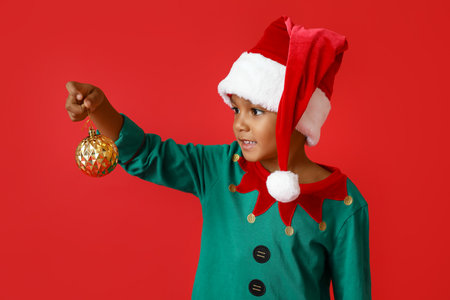 Little African-American boy with Christmas ball on red background